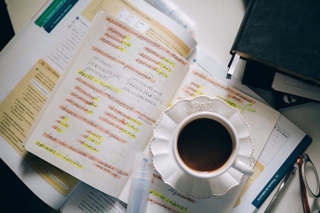 Uma imagem de um livro com palavras estrangeiras e sua tradução em uma mesa com uma xícara de café.