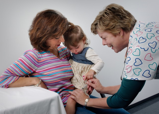 Uma pessoa segura uma criança pequena que recebe uma injeção.
