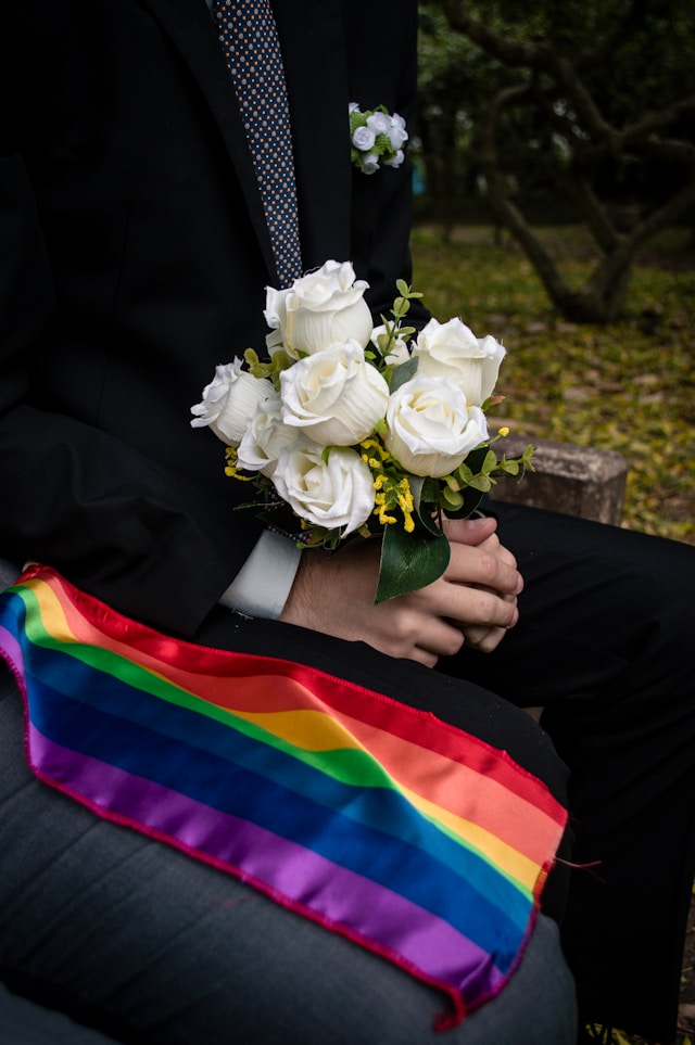 Qual é o país mais fácil para adotar? 4 Um close-up de um noivo segurando um buquê de casamento de rosas brancas ao lado de uma bandeira do arco-íris.