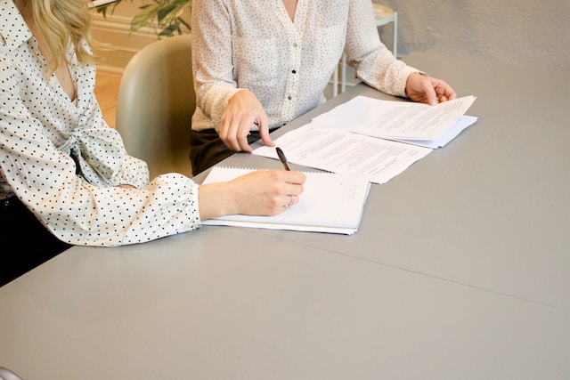 Zwei Personen lesen Geschäftsdokumente, während eine Person Notizen macht.