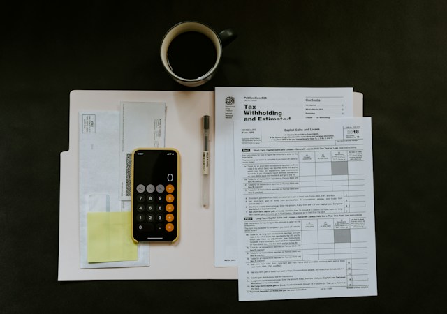 Ein Bild von mehreren Steuerunterlagen auf einem Tisch mit einem Telefon und einer Tasse Kaffee auf einem Tisch.