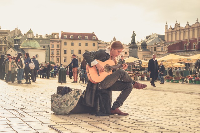 Eine Person sitzt mitten auf einer Straße voller Menschen und spielt Gitarre.
