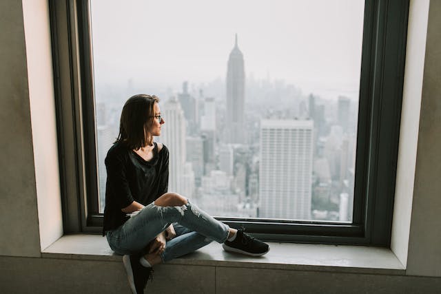 Dónde traducir documentos jurídicos 4 Mujer con chaqueta negra y vaqueros azules sentada en una ventana de Nueva York con vistas.