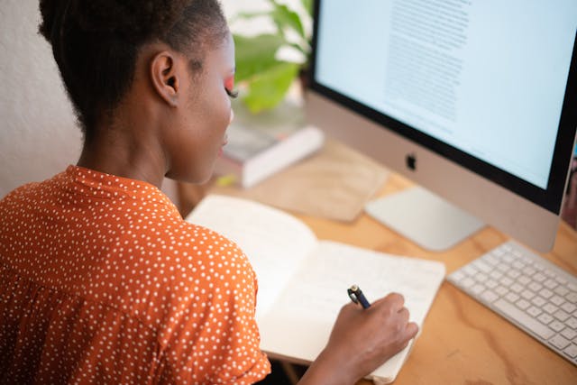 Services de traduction en 24 heures : Obtenir des résultats en un jour 5 Une femme écrivant dans un carnet et travaillant sur un ordinateur à un bureau pour symboliser les services de traduction.