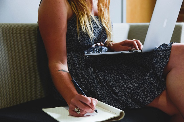 Emplois de traduction à domicile : Conseils pour développer votre carrière 5 Une personne place un ordinateur portable argenté sur sa jambe et écrit dans un livre tout en étant assise sur un canapé.