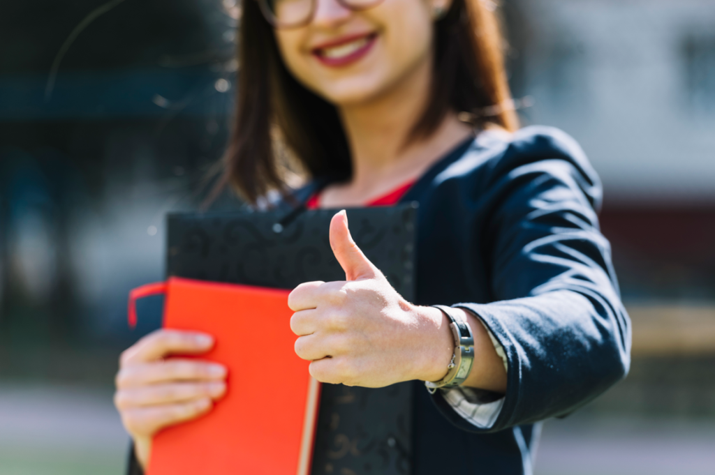 Une femme heureuse, avec des documents, qui lève le pouce.