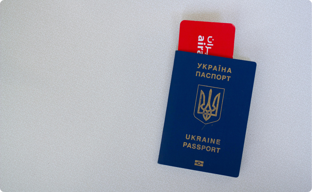 Blue Ukrainian passport with a red plane ticket visible inside it on a gray background.