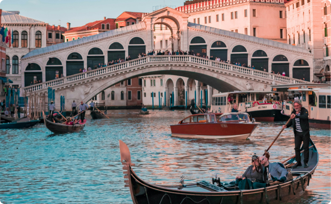 The Rialto bridge in Venice, Italy, on a sunny day with gondolas in the river symbolizing Italian language and culture.