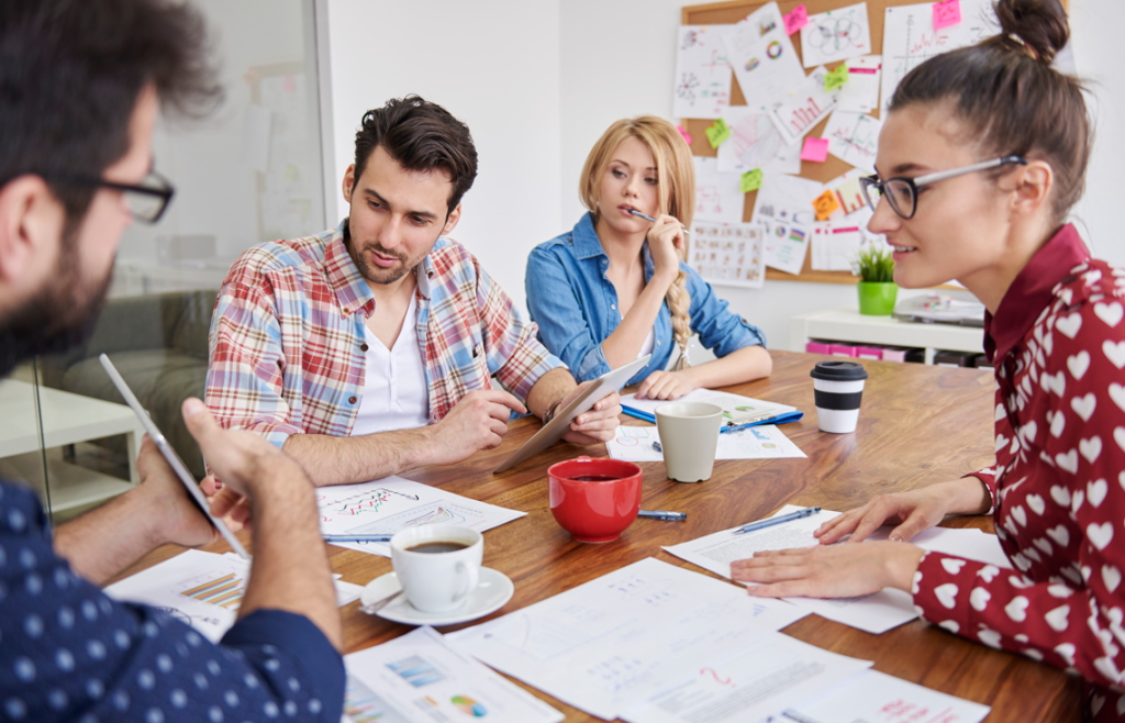 Un gruppo di quattro persone che discute intorno a un tavolo con grafici, documenti e tazze di caffè.