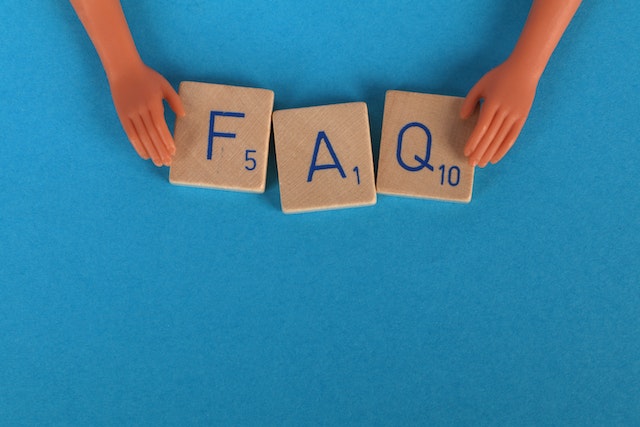 A close-up shot of Scrabble tiles spelling FAQ on a blue surface.