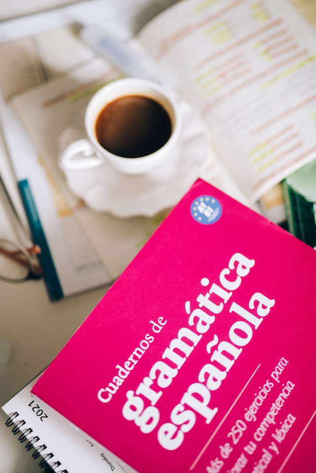 A Spanish grammar book on a desk calendar beside a cup of coffee.