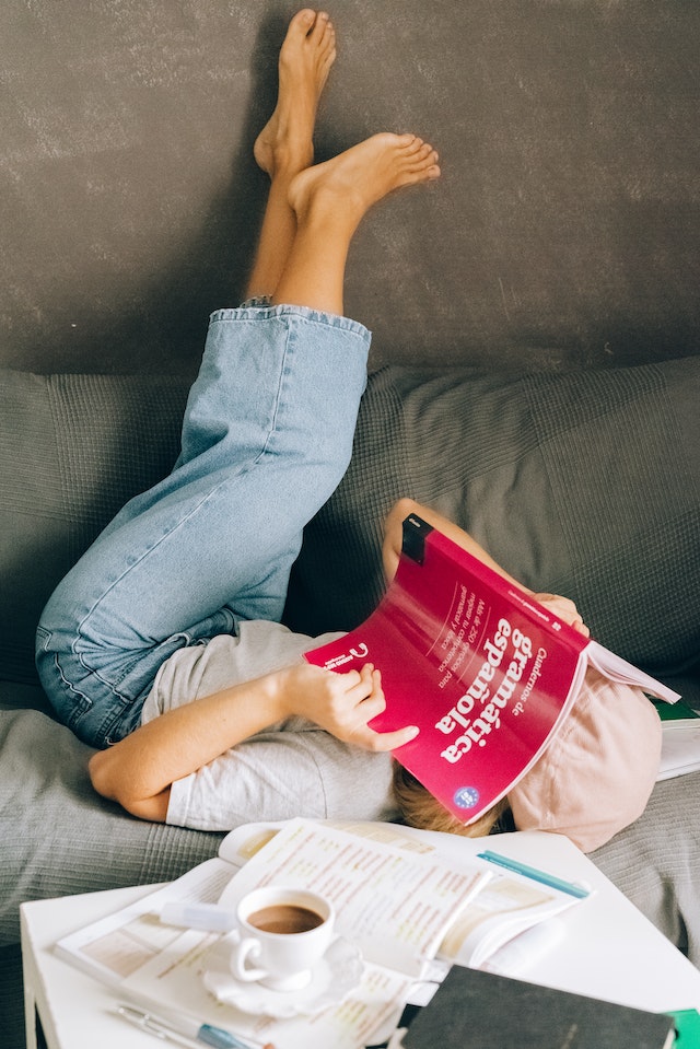 Woman lying upside down on a couch reading a book about translating spanish.