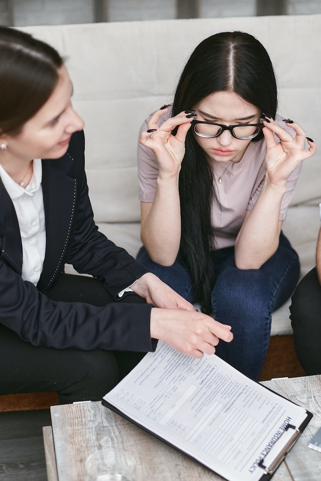 Professional helping a woman with glasses to sign an official document.