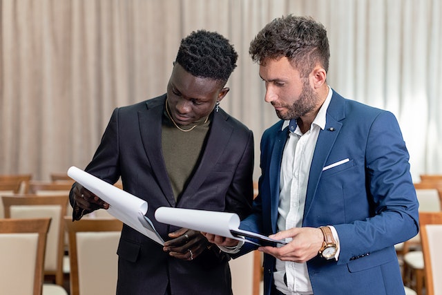 Businessmen in black and blue suit having a conversation while holding documents.