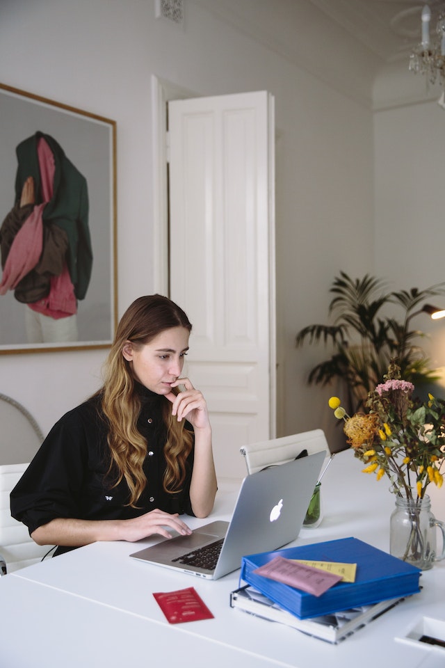 Woman in a black turtleneck sitting at a white table and translating a birth certificate on a laptop.