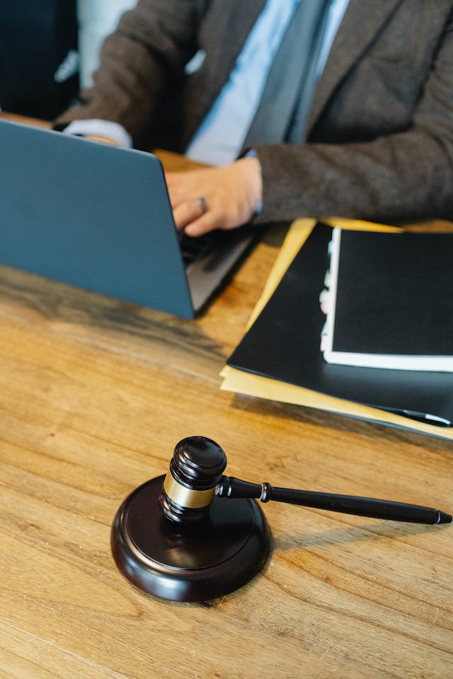 Wooden gavel on the wooden surface next to a man working on a computer