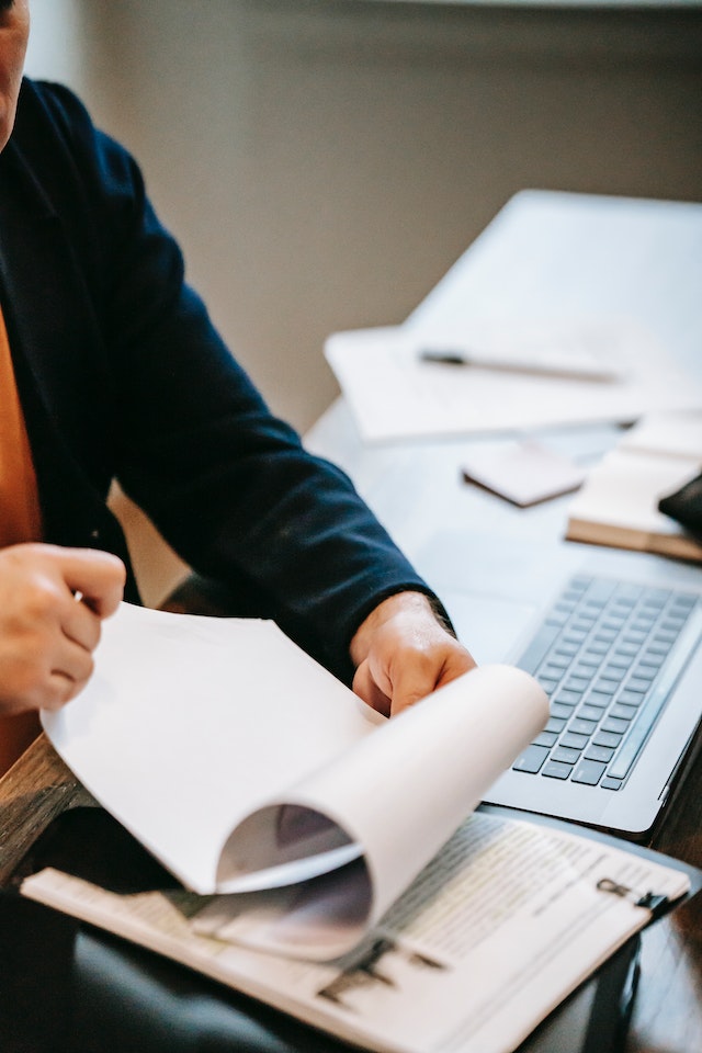 Person flipping pages of a document pamphlet on top of a messy work space.