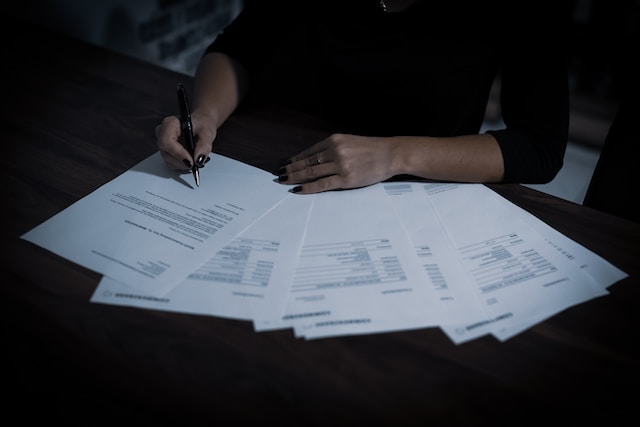 A photograph of a person signing several documents on a table.