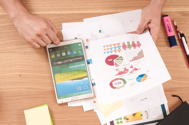 A picture of someone reading several printed graphs on a table with a phone and pens.