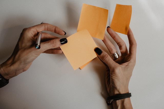 A picture of a person holding several brown sticky notes.