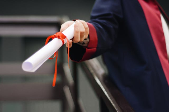 A picture of a person holding a folded certificate tied with a ribbon.