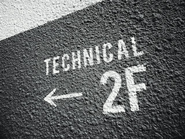 A picture of a rough black wall with the text “TECHNICAL 2F” painted in white.