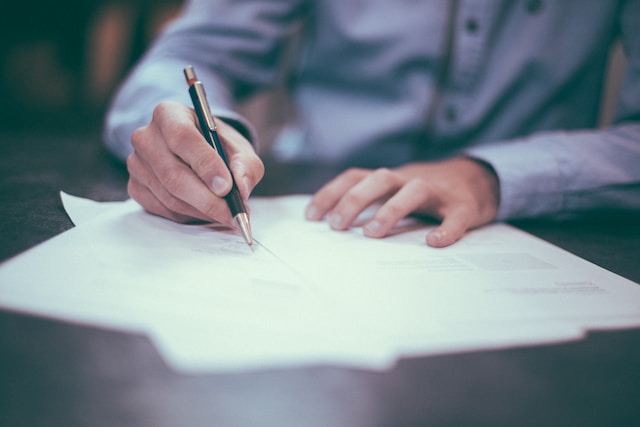 A photograph of a person writing into paper documents on a table.