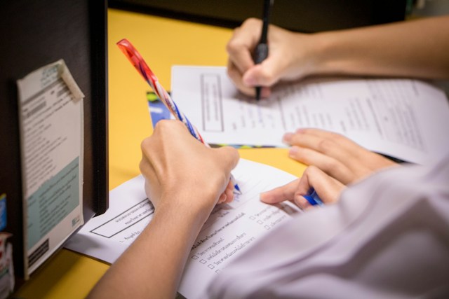 A picture of two people filling out two documents on a desk.