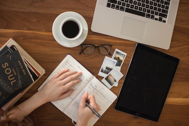 A writer writing in a notebook next to a cup of coffee