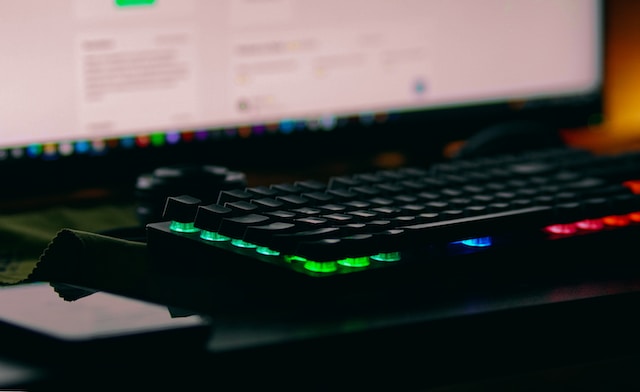 A picture of a computer keyboard on a desk with a monitor ahead.