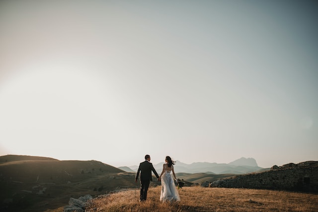A photograph of a bride and a groom walking on a hill. 
