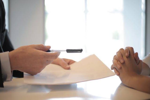 A photograph of a person handing a pen to another person.