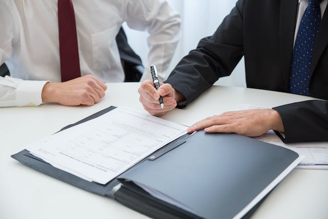 A photo of someone signing a document while another person looks on.