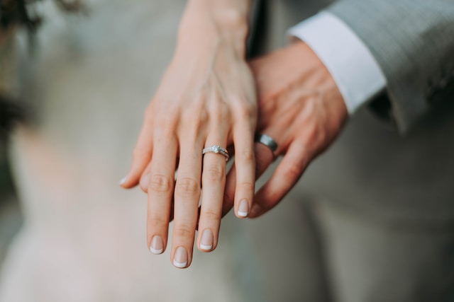 A picture of two people with wedding rings holding hands.
