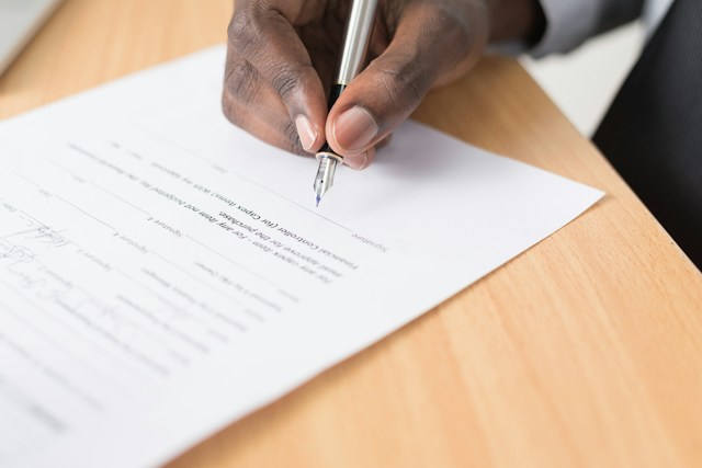 A person signing an official document on a wooden table. 