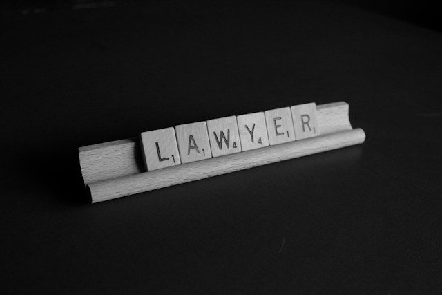 Gray Scrabble tiles on a black background arranged on the rack to spell “LAWYER.”