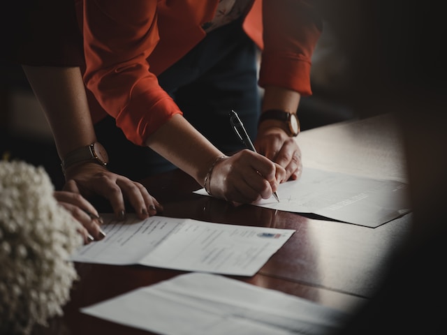 Two people are signing documents on a wooden table.