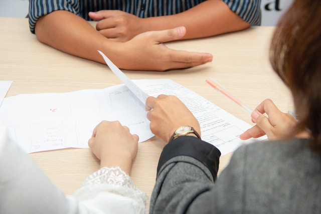 Two seated people are explaining the documents on their table to the person seated in front of them.