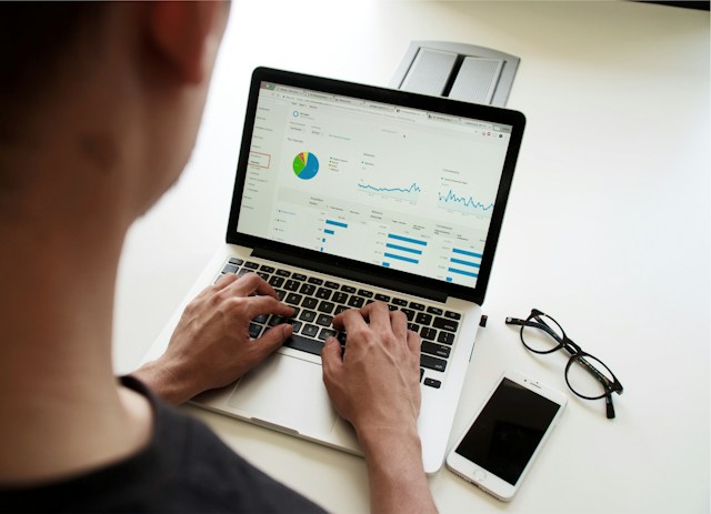 A man uses a Macbook that displays analytical data.
