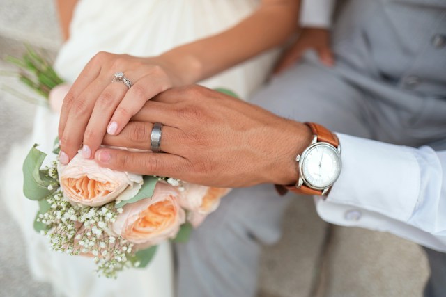 A man and woman holding hands while displaying their wedding rings.
