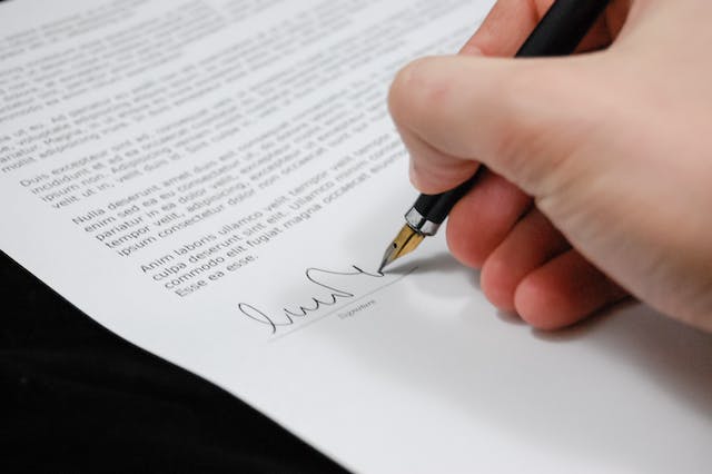 A person signing a document with a pen.
