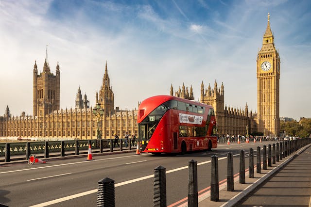 A red hop-on-hop-off bus in London drives past the Big Ben.