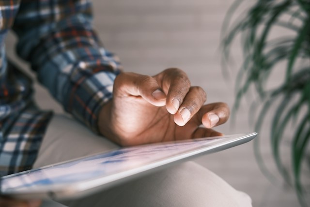 A person in a blue and white plaid long-sleeved shirt holds a silver digital tablet.
