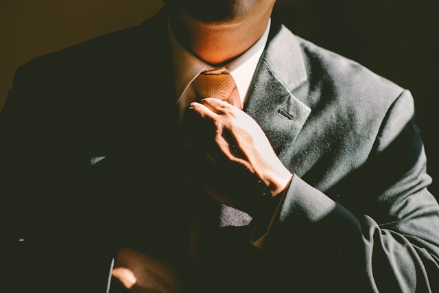 A man in a black suit adjusting his brown tie.
