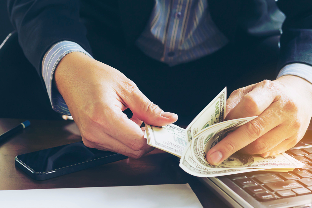 A person counts dollar banknotes on a computer keyboard.