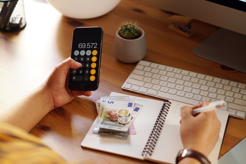 A person uses a calculator and writes in a book with money placed on it.