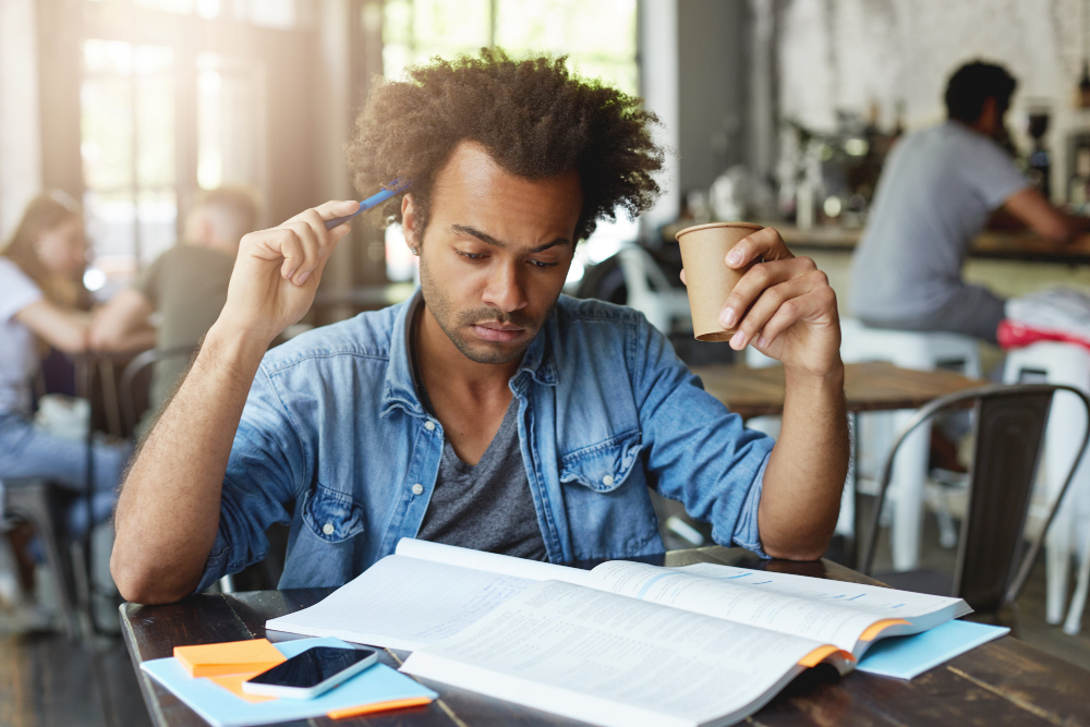 A person scratches their head with a pen and concentrates on a book.