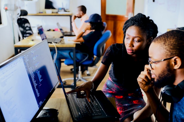 A lady and a man working together in an office on a computer system. 
