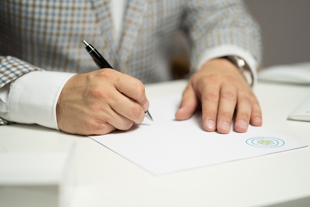 A man in a checkered suit writes on a printed paper.

