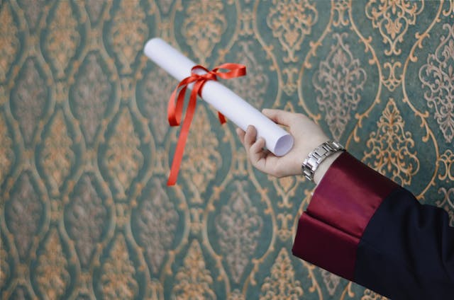 A person holds a folded certificate with a red ribbon.